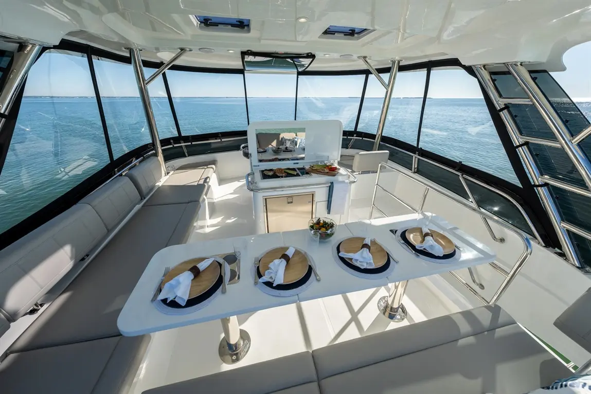 Luxury yacht interior with dining setup, featuring plates, cutlery, and a scenic view of calm waters through large windows.